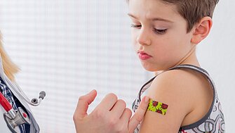 Ein kleiner Junge bekommt nach dem Impfen ein buntes Pflaster auf den Arm geklebt.